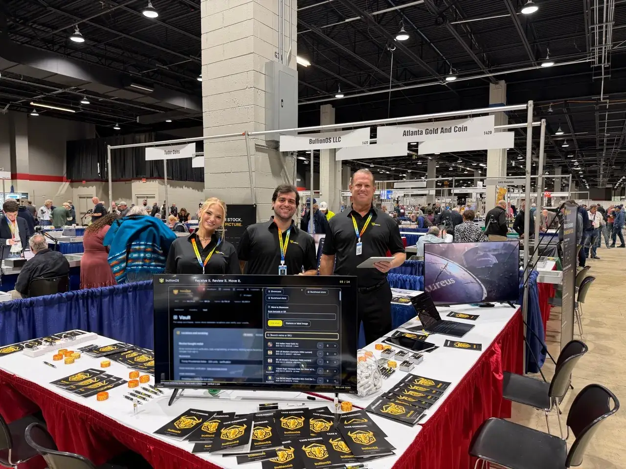 Lilly L., Henrique L. and Brock T. at the bullionOS booth at the 2026 Great American Coin & Collectibles Show (GACC) in Rosemont, IL, with bullionOS dealer software on screen